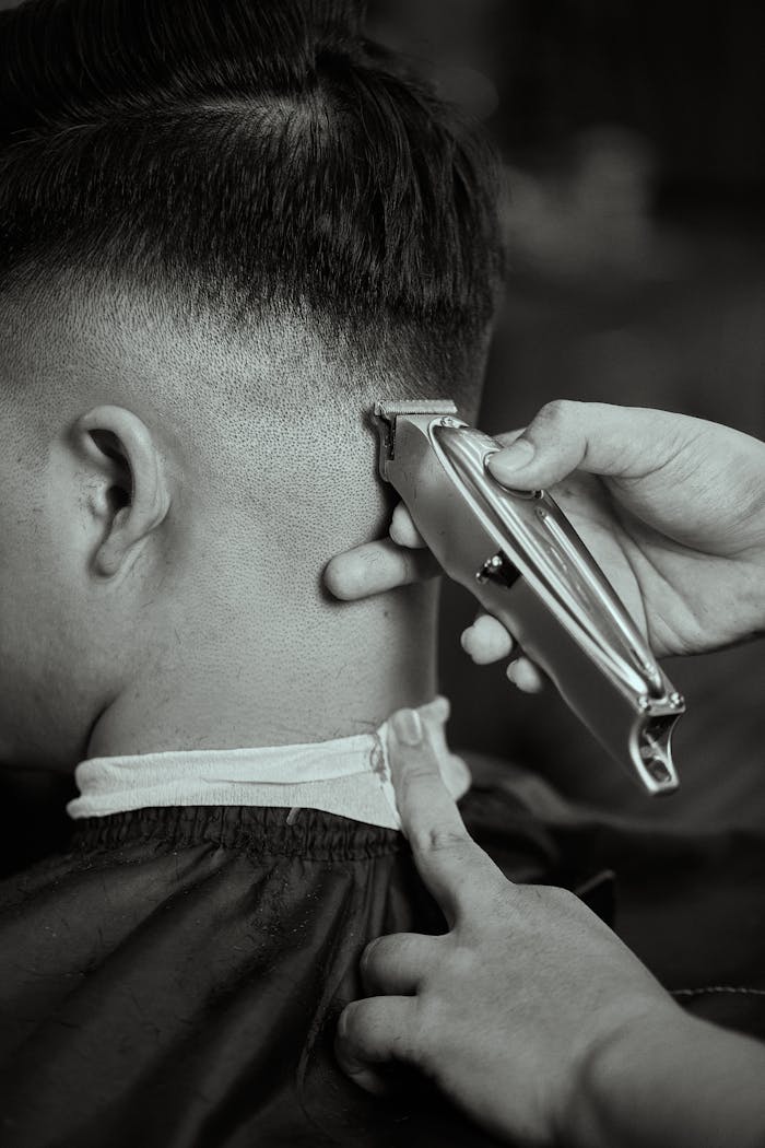 Detailed black and white close-up of a barber trimming a mans hair with clippers.